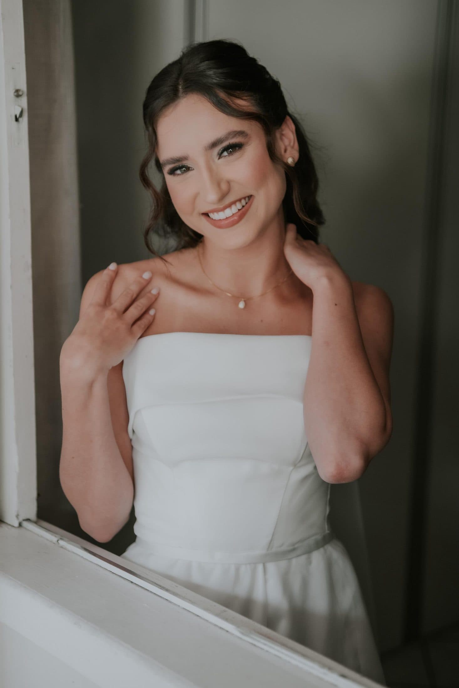 Noiva sorrindo junto à janela, com pele luminosa e coque baixo
