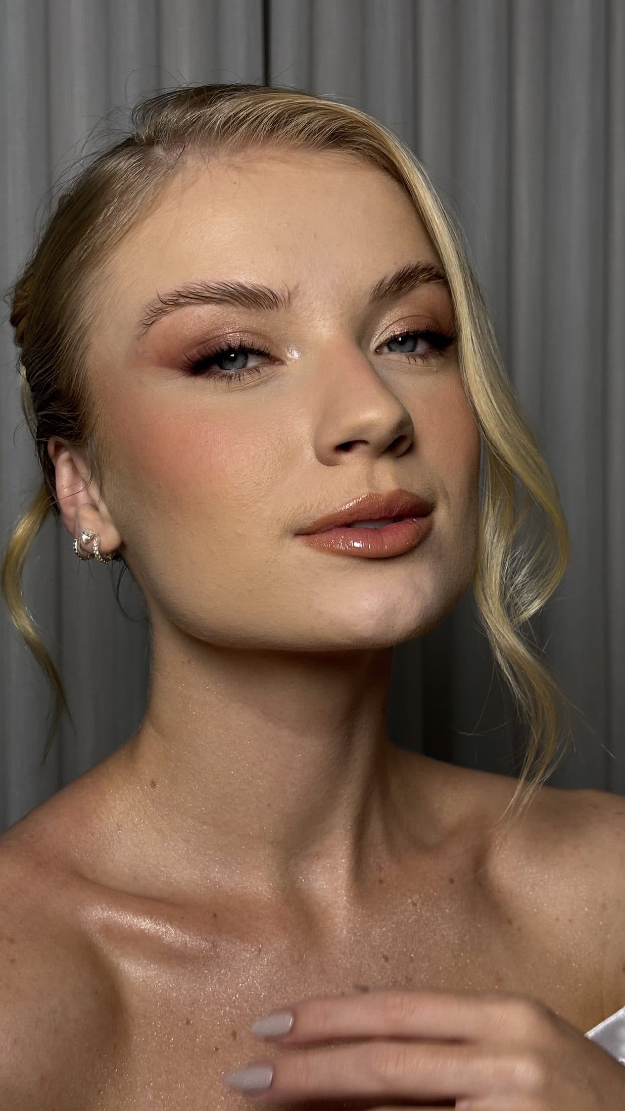 Cliente loira com pele iluminada, blush pêssego e cabelo preso com mechas soltas